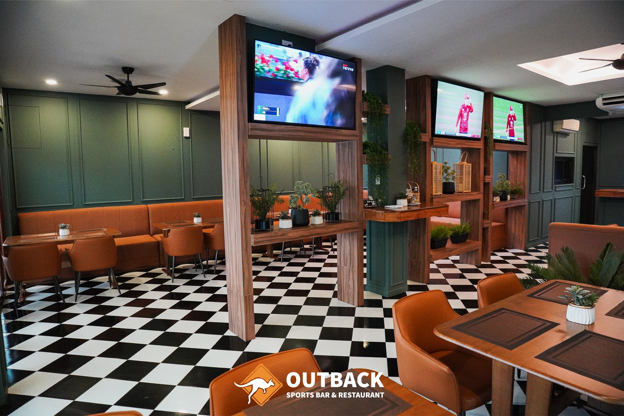 Outback dining room with leather booths, plants and a wall of sport screens